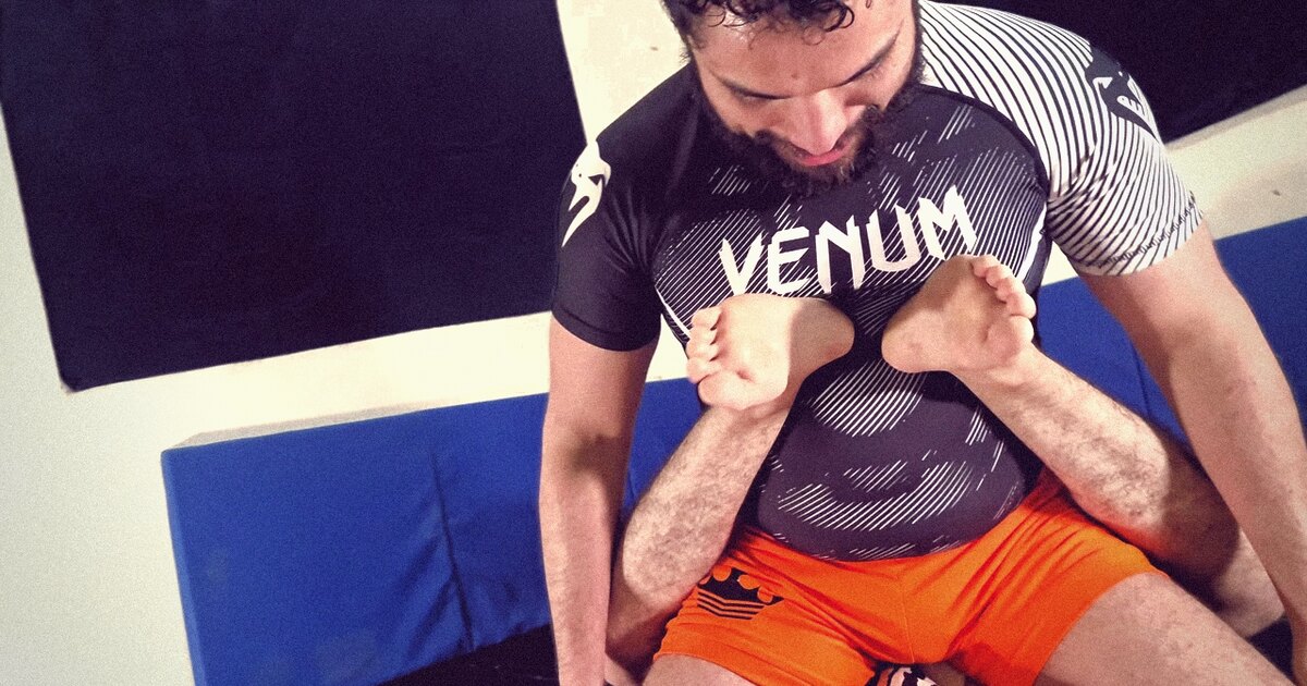 Robgrappler, con rashguard Venum y short naranja, presiona contra los pies de su rival durante una lucha de sumisión sin guion.
